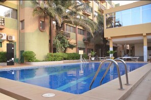 A swimming pool with a clear blue water, surrounded by a building with balconies and greenery.