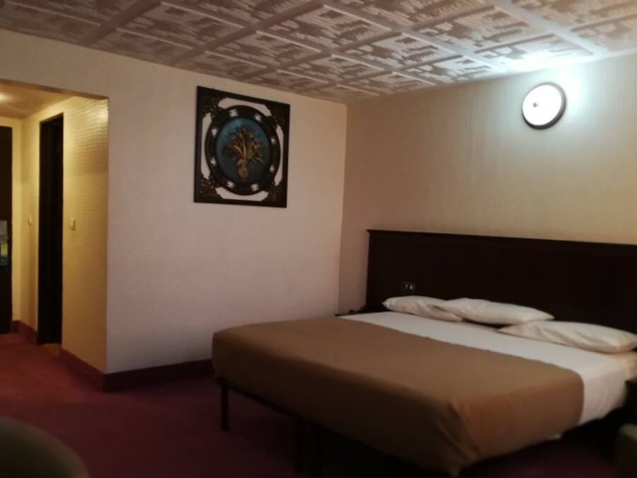 A hotel room with a bed, a door, and a wall-mounted light fixture.