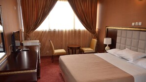 A hotel room with a large bed, two armchairs, a small table, a desk with a lamp, and a mirror. - Hotel Palm Beach (Ouagadougou)