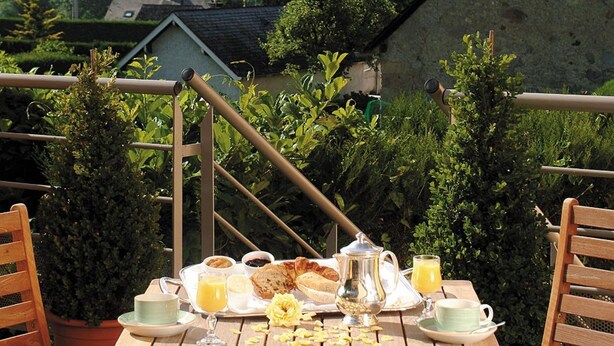 A table set for breakfast with a mountain view, surrounded by potted plants and wooden chairs.
