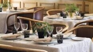 A dining area with tables set for two, each with a white tablecloth, candles, and small plants. A large mirror with a decorative frame hangs on the wall above the tables.