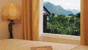 A bed with a book and a lamp, a window with curtains, and a view of mountains.