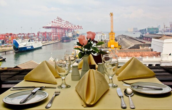 A table set for dining with a view of a port and cranes in the background. - Grand Oriental Hotel (Colombo)