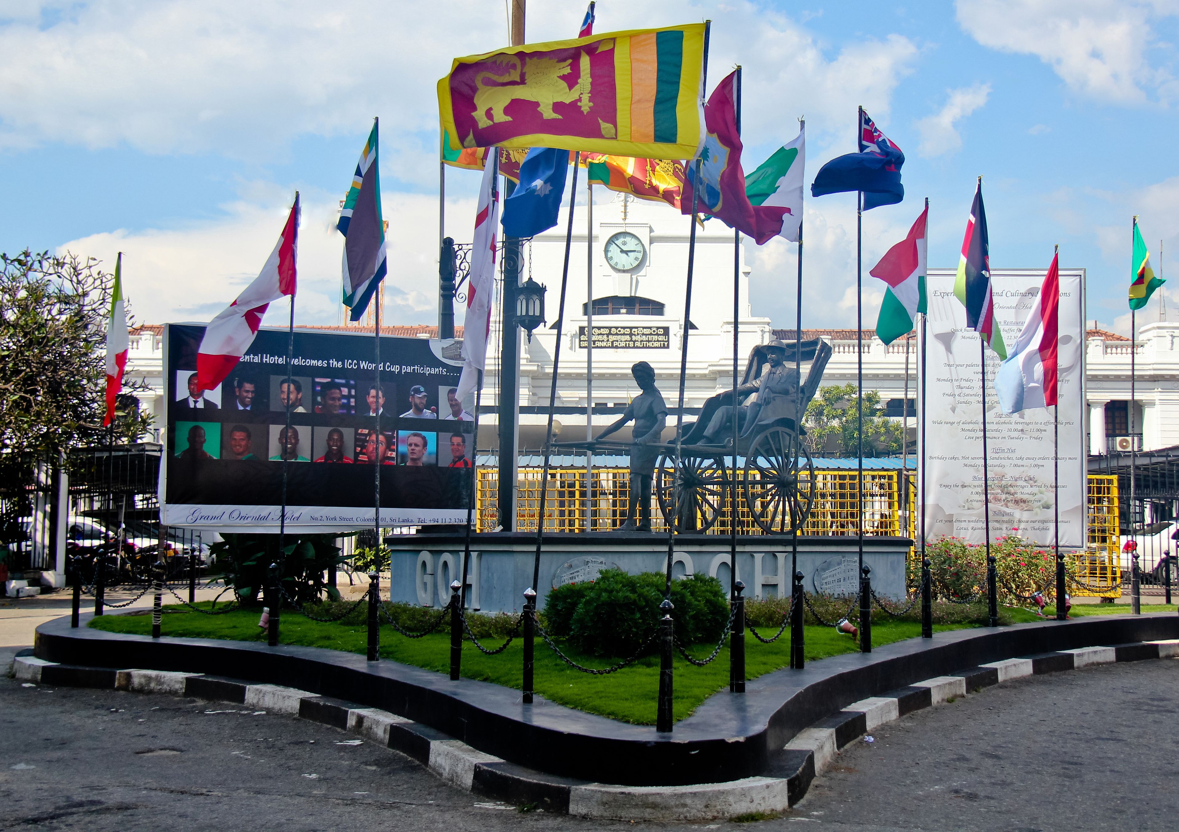 A monument with multiple flags, a clock tower, and a statue in the background.