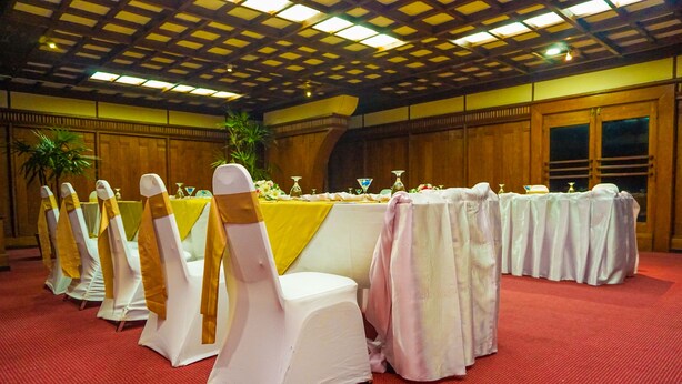 A banquet hall with rows of tables, each with a white tablecloth and a chair with a white cover and a gold sash. - Grand Oriental Hotel (Colombo)