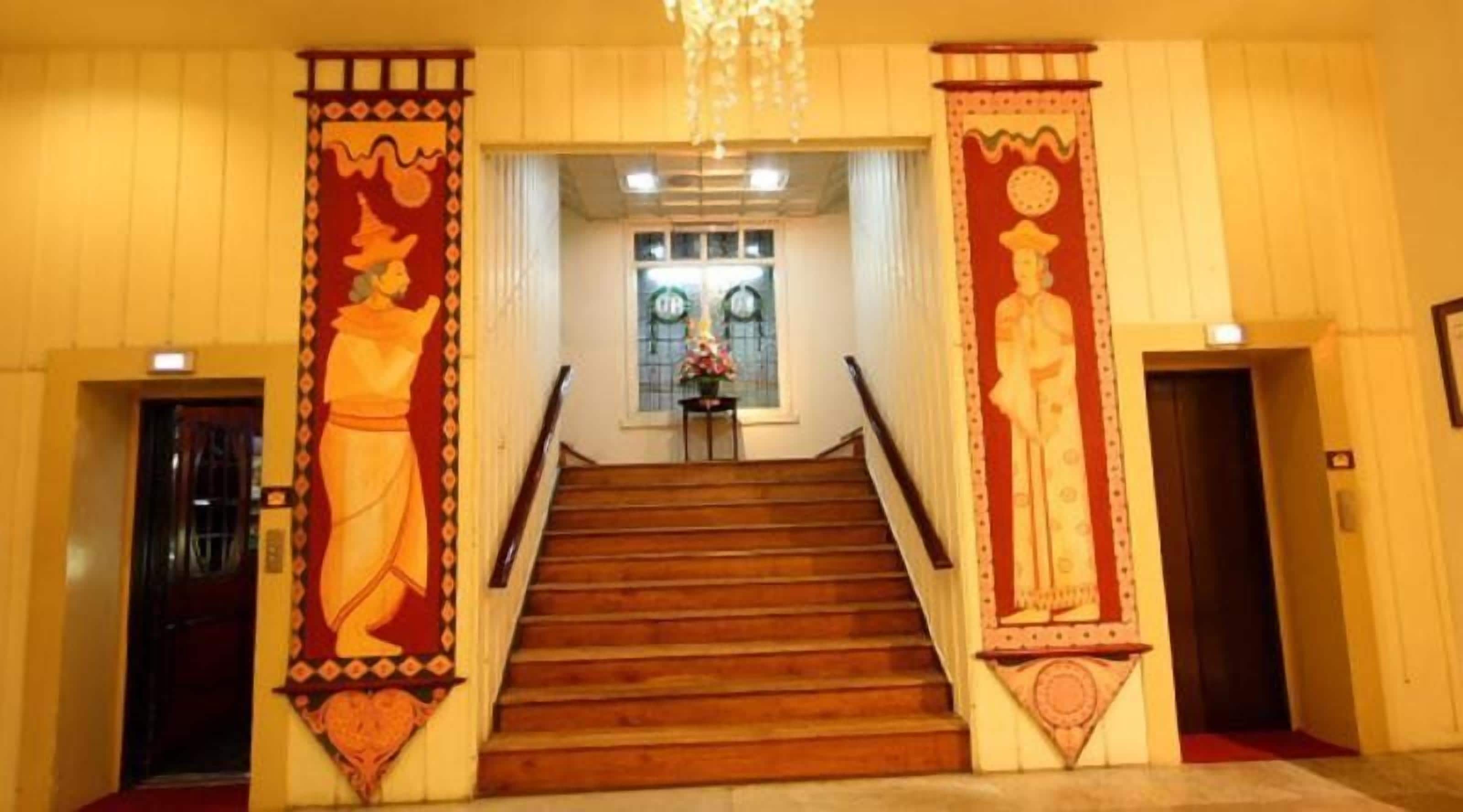 A staircase with wooden steps leading to a landing area, flanked by two large decorative panels with figures.