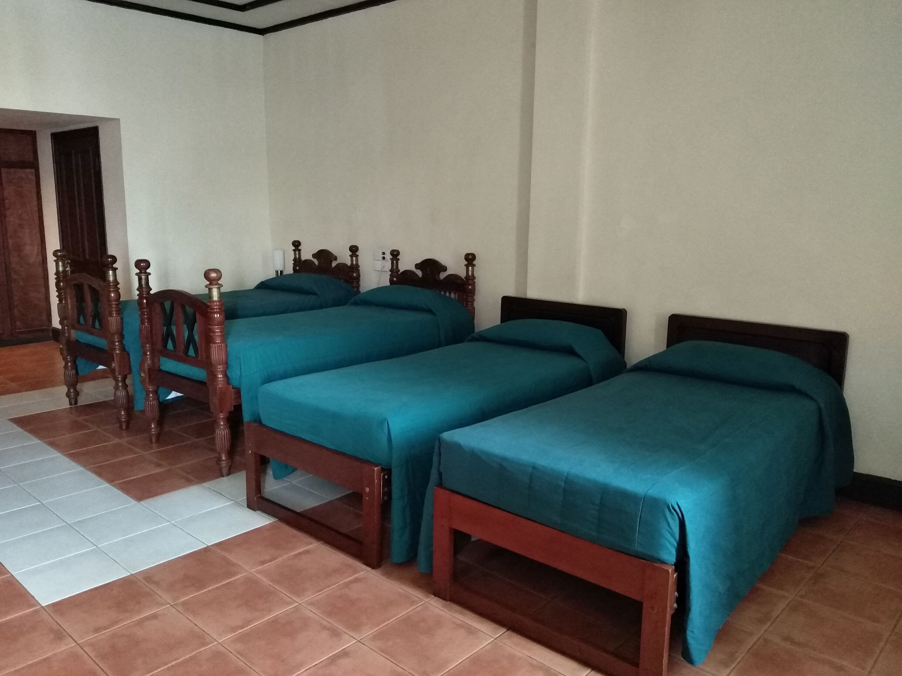 A room with four wooden beds, each with a teal bedspread, and a wooden chair with a green cushion.