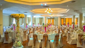 Un salón de banquetes con mesas redondas, sillas blancas y centros de mesa florales.