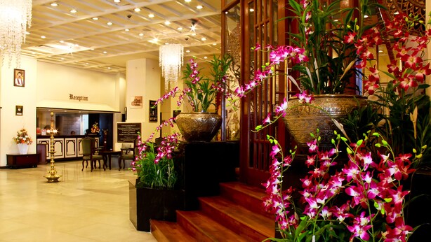 Zona de recepción con candelabro, mostrador y orquídeas en macetas.
