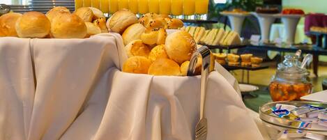 A buffet with various breads, pastries, and a glass of orange juice.