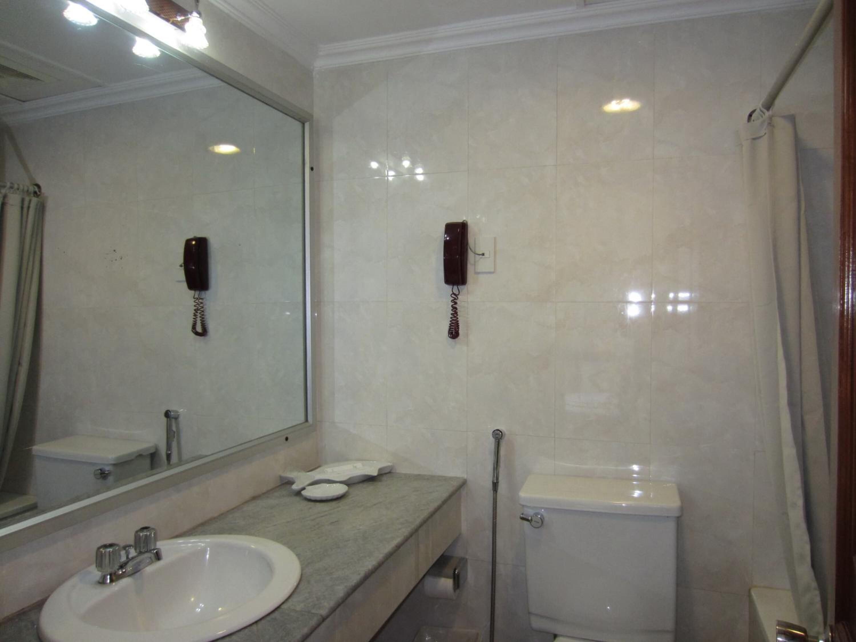 A bathroom with a sink, mirror, toilet, and two phones mounted on the wall.