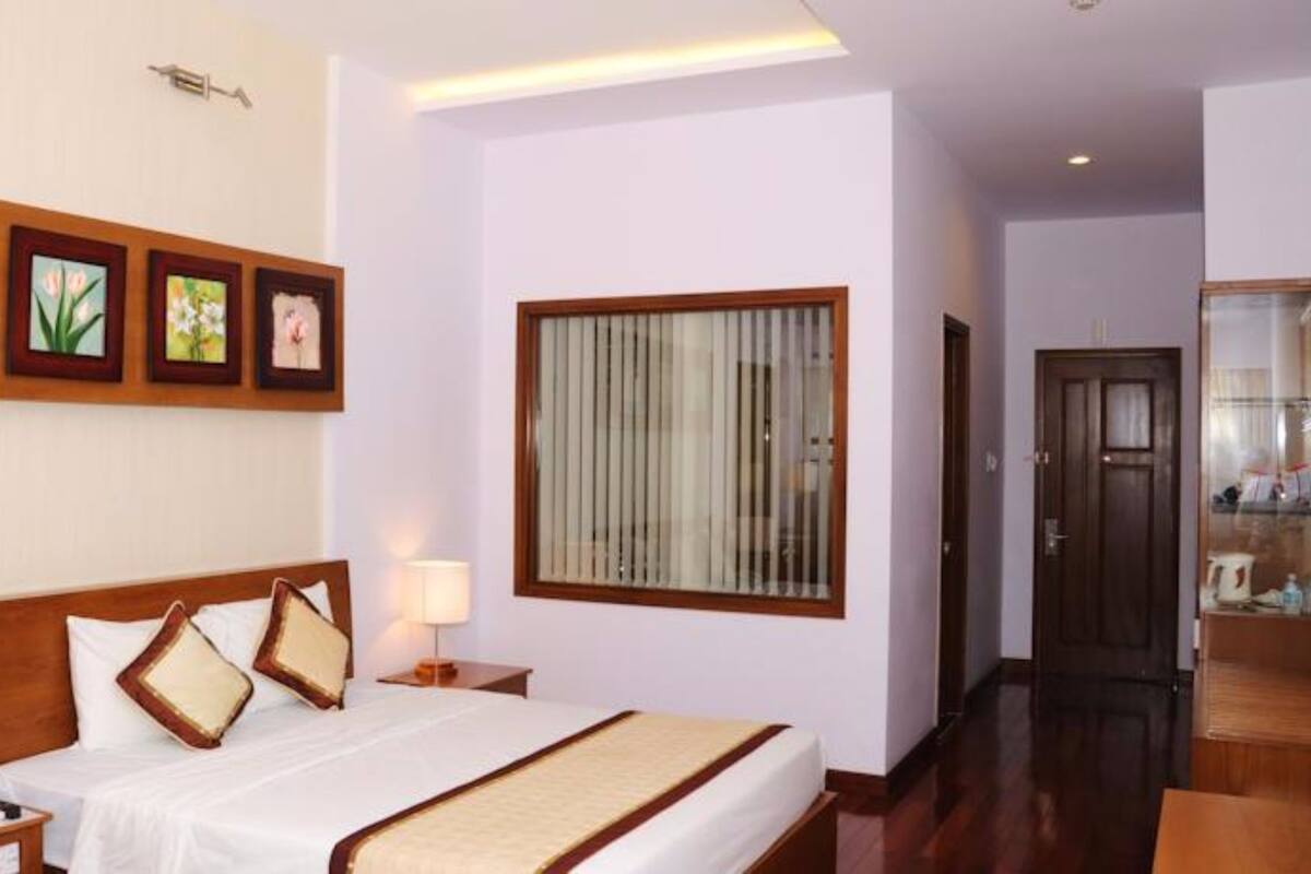 A hotel room with a bed, bedside tables, a window with blinds, and framed pictures on the wall.