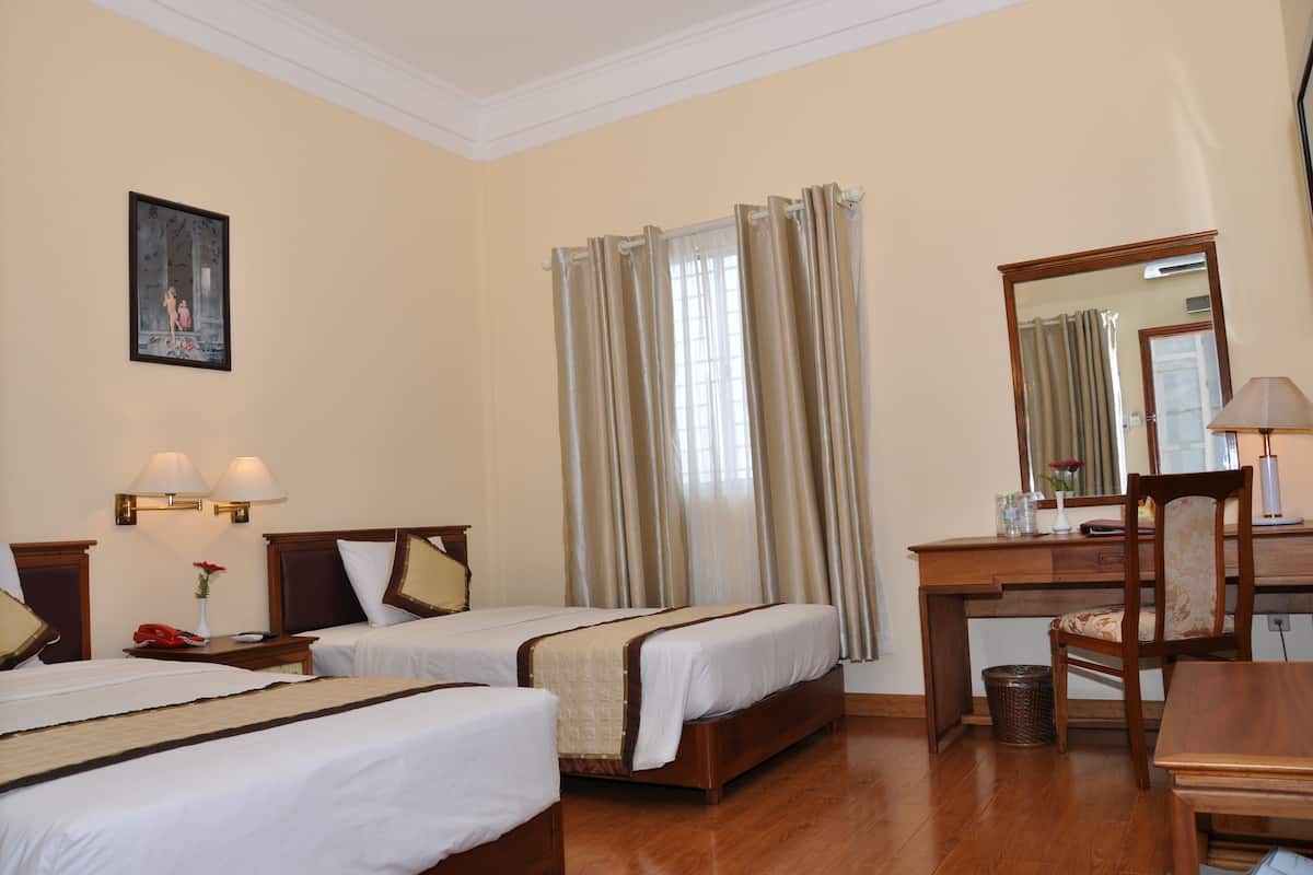 A hotel room with two single beds, a desk with a chair, a mirror, and a lamp.