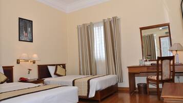 Quarto de hotel com duas camas de solteiro, uma escrivaninha com cadeira, um espelho e um abajur.