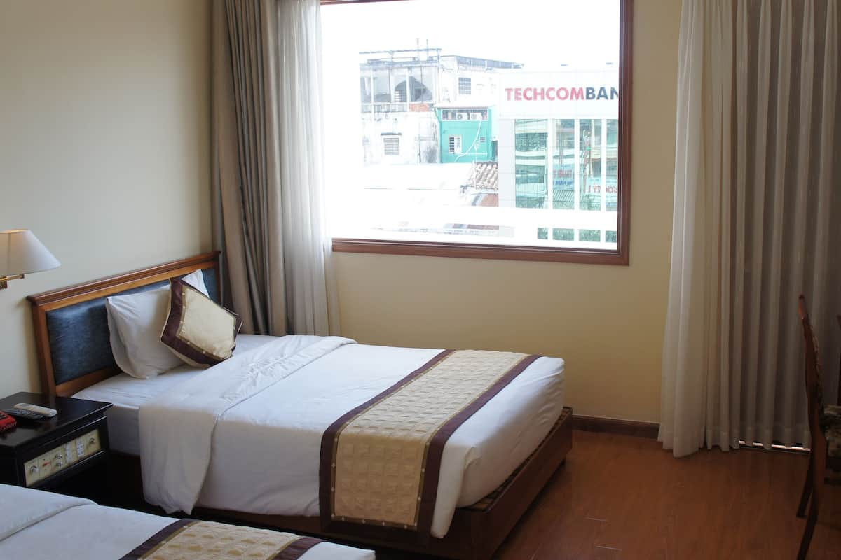 A hotel room with a bed, a nightstand, a desk, a lamp, and a window with curtains.
