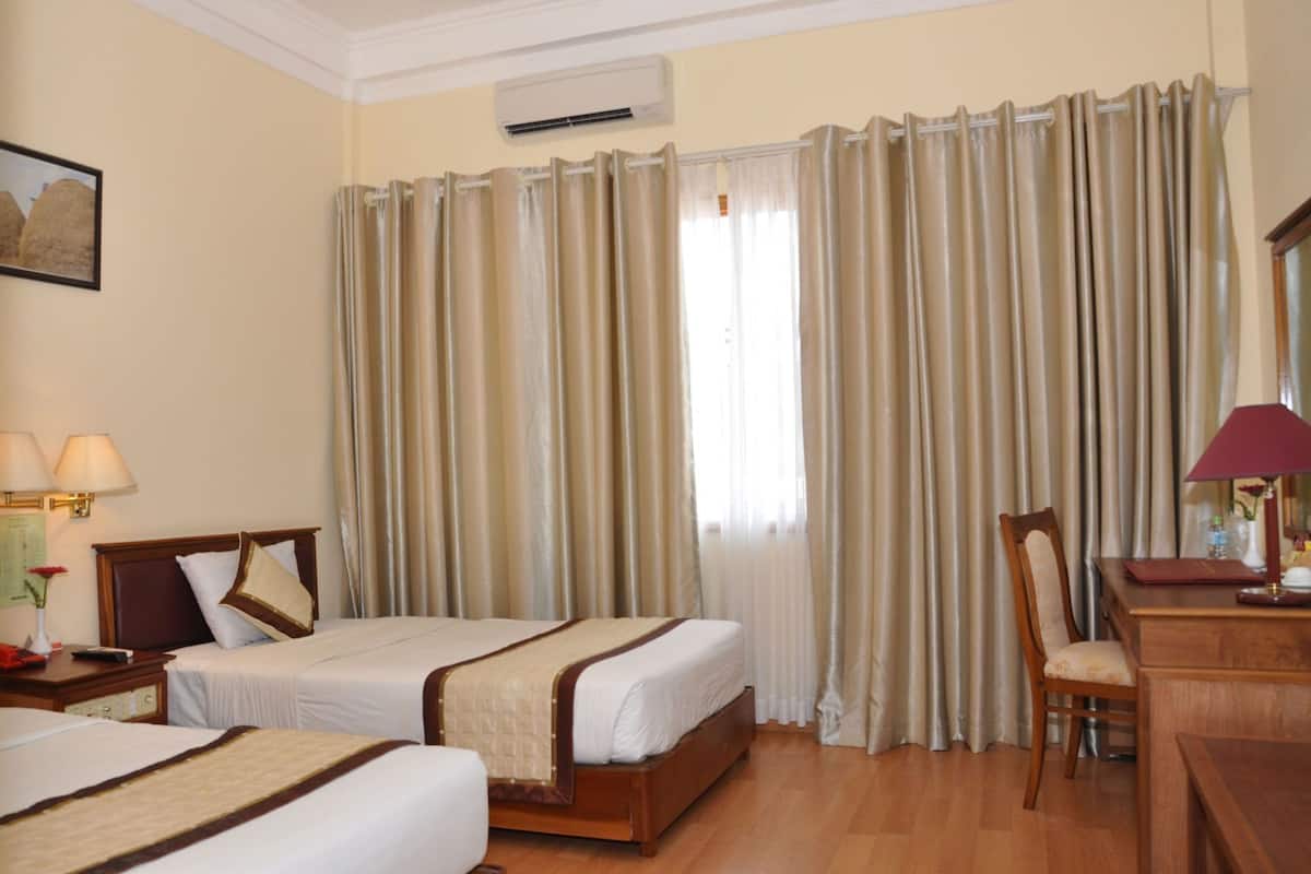 A hotel room with two beds, a desk, a chair, a lamp, and a window with curtains.