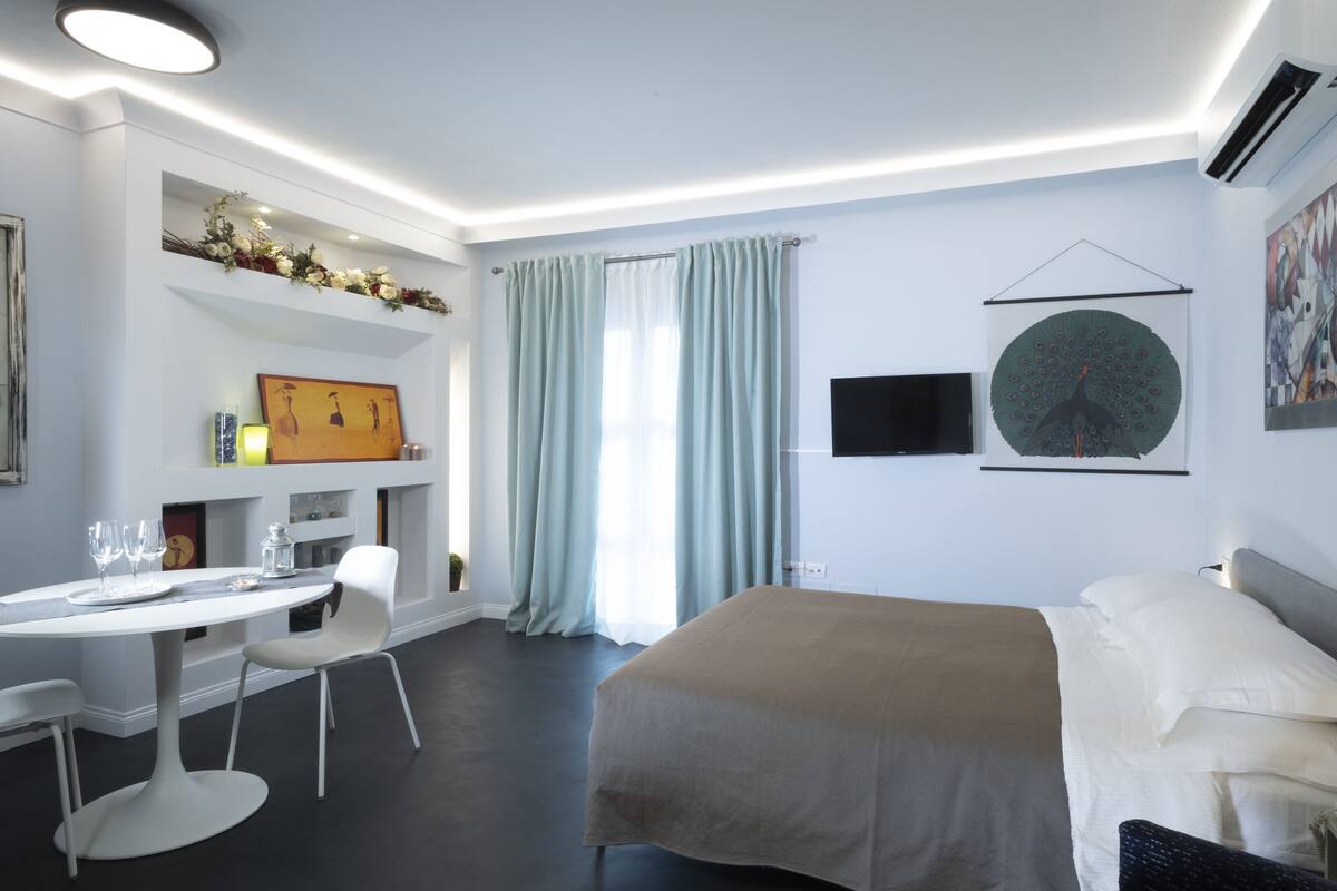Quarto de hotel moderno com uma cama, uma secretária com cadeiras, uma televisão de tela plana e obras de arte nas paredes.