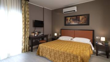 A hotel room with a bed, a desk, a chair, a nightstand, a TV, and a painting on the wall.