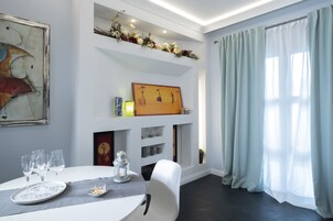 Un comedor con una mesa blanca, vasos transparentes, una vela y una estantería decorada con flores.