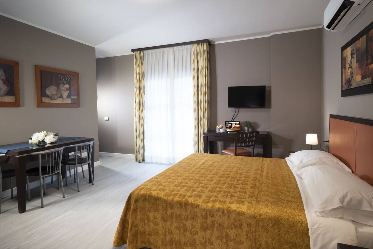 Quarto de hotel com cama, escrivaninha e televisão.