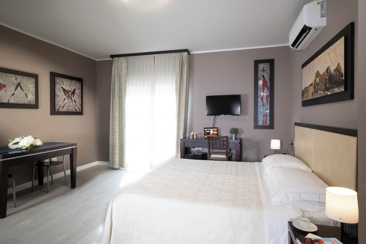 Quarto de hotel com cama, secretária, cadeira, televisão e obras de arte nas paredes.