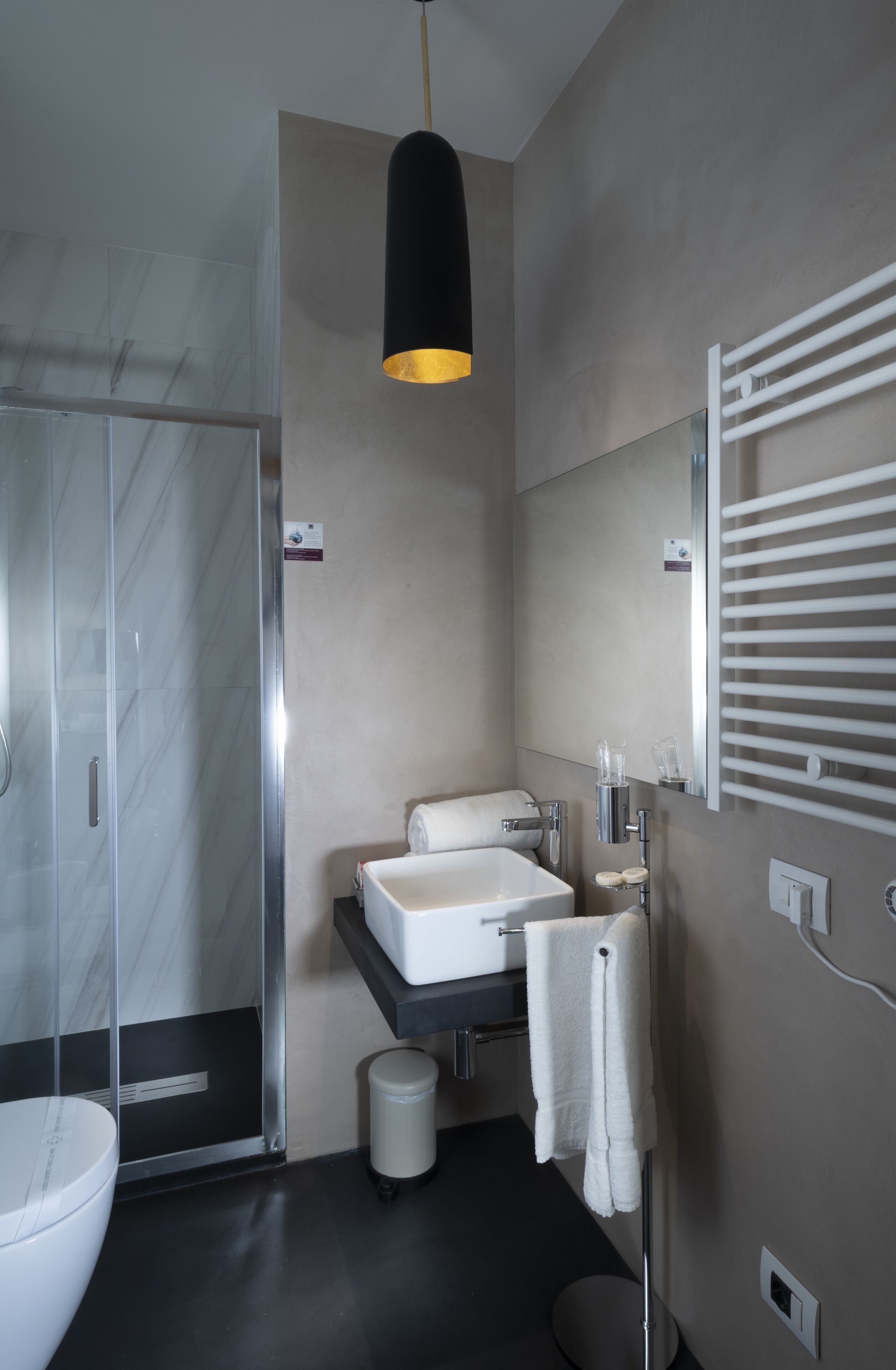 A modern bathroom with a glass shower enclosure, a white sink, and a towel rack.