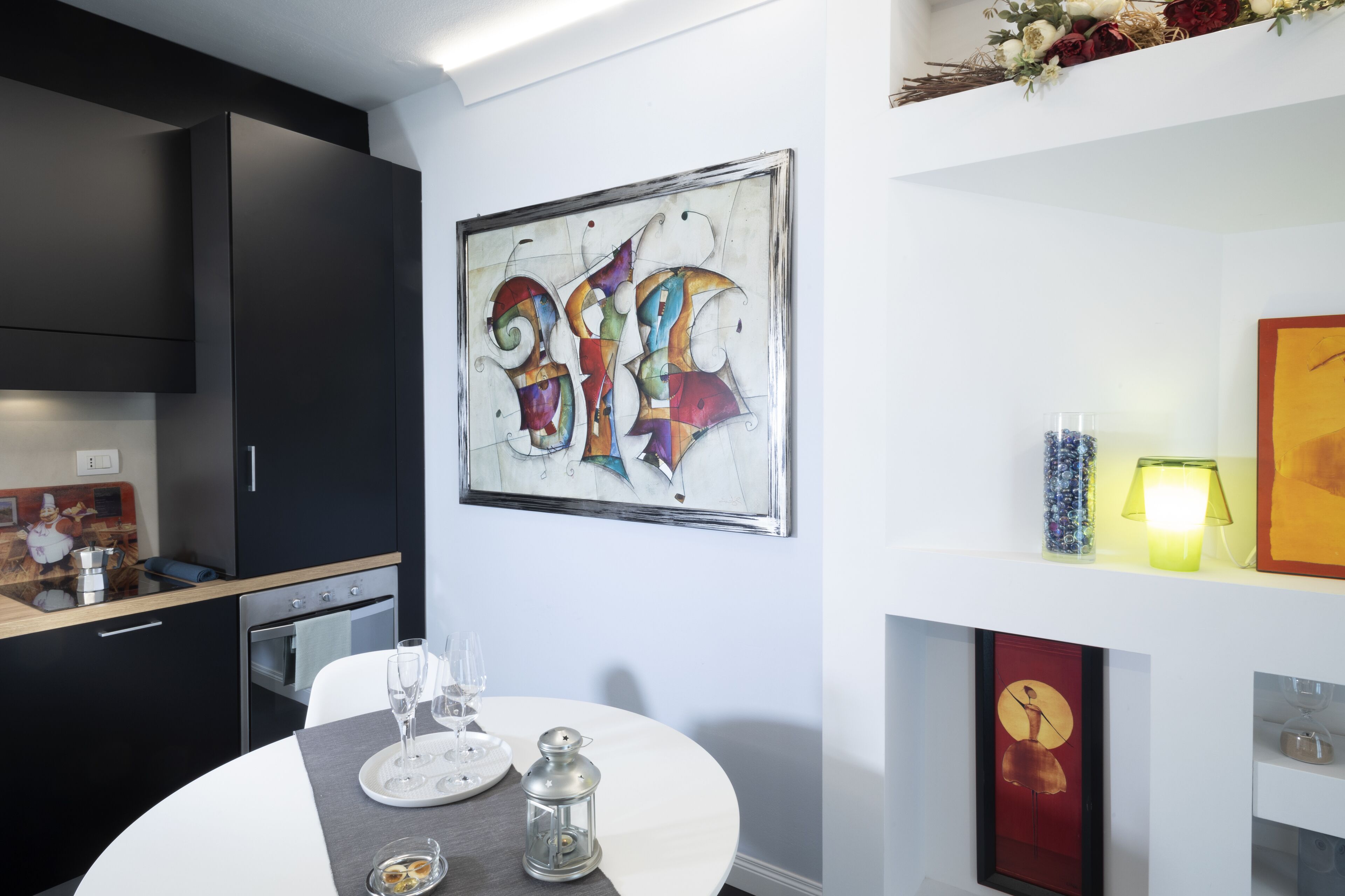 A modern kitchen with dark cabinetry, a dining table with a white tablecloth, and a colorful abstract painting on the wall.