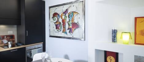 A modern kitchen with dark cabinetry, a dining table with a white tablecloth, and a colorful abstract painting on the wall.
