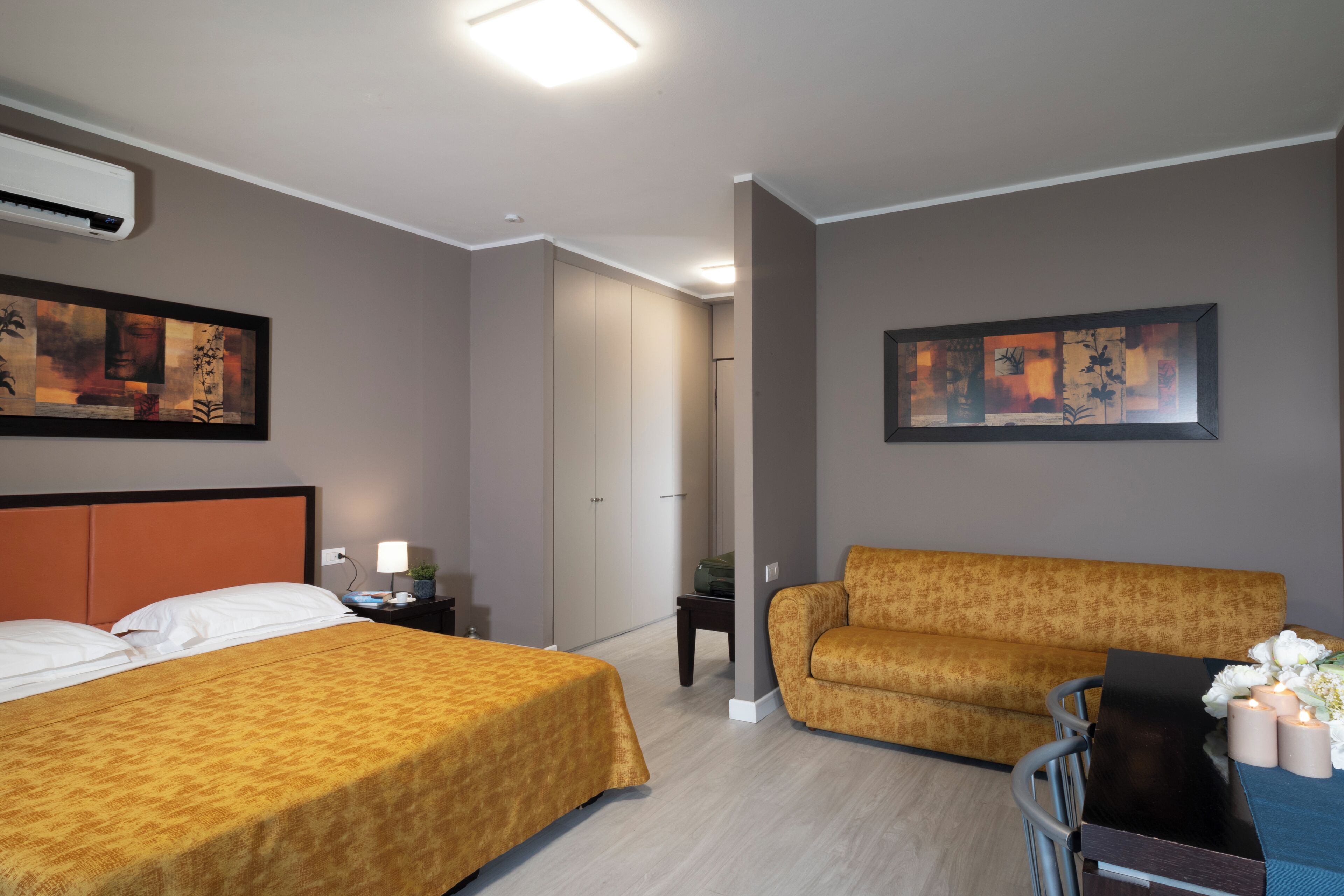 Une chambre d’hôtel avec deux lits, un canapé, une table avec des bougies et des œuvres d’art accrochées aux murs.