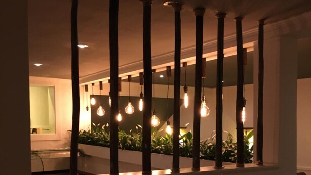 A room with a modern design, featuring a large window with multiple light bulbs and a view of a balcony with plants. - Hotel Fritz (Valwig)