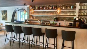 A bar area with a counter, stools, and shelves of bottles. - Hotel Fritz (Valwig)