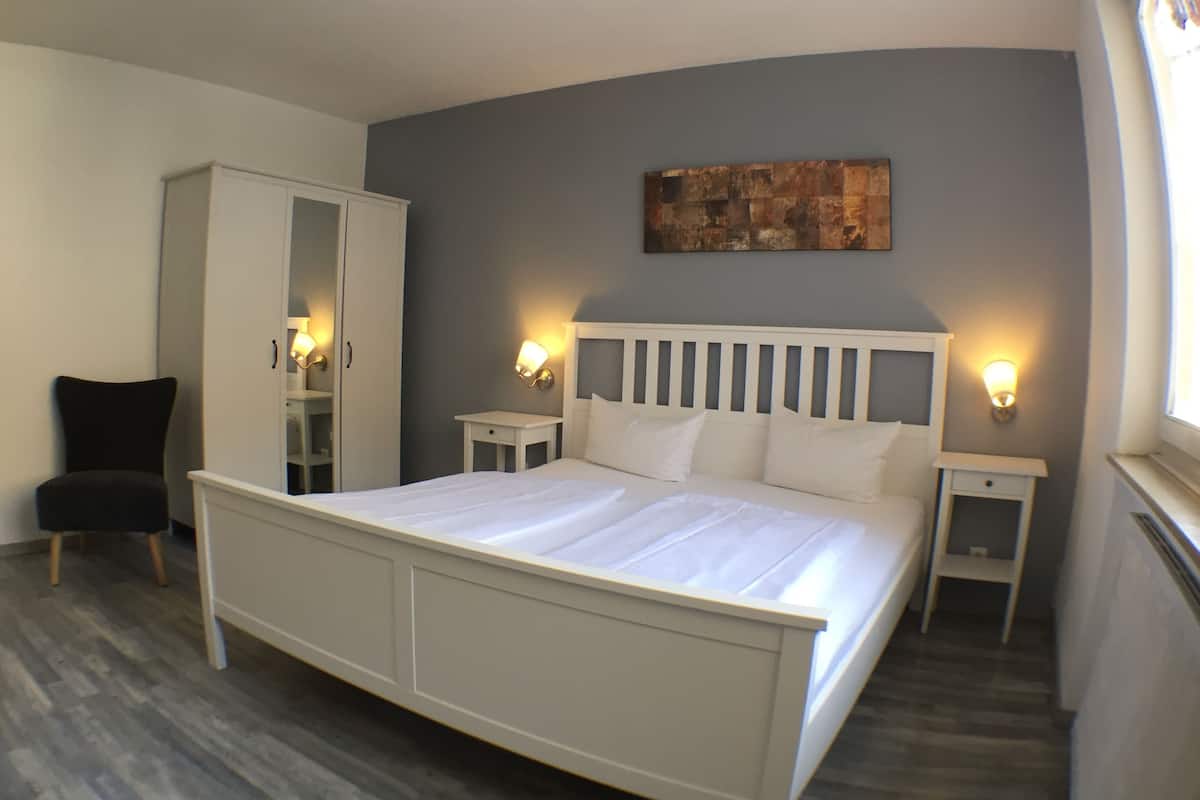 Une chambre avec un grand lit, une armoire, une chaise et des lampes de chevet.