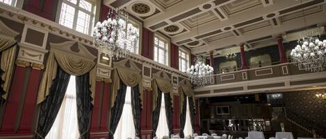 A grand ballroom with ornate chandeliers, high ceilings, and elegant drapery.