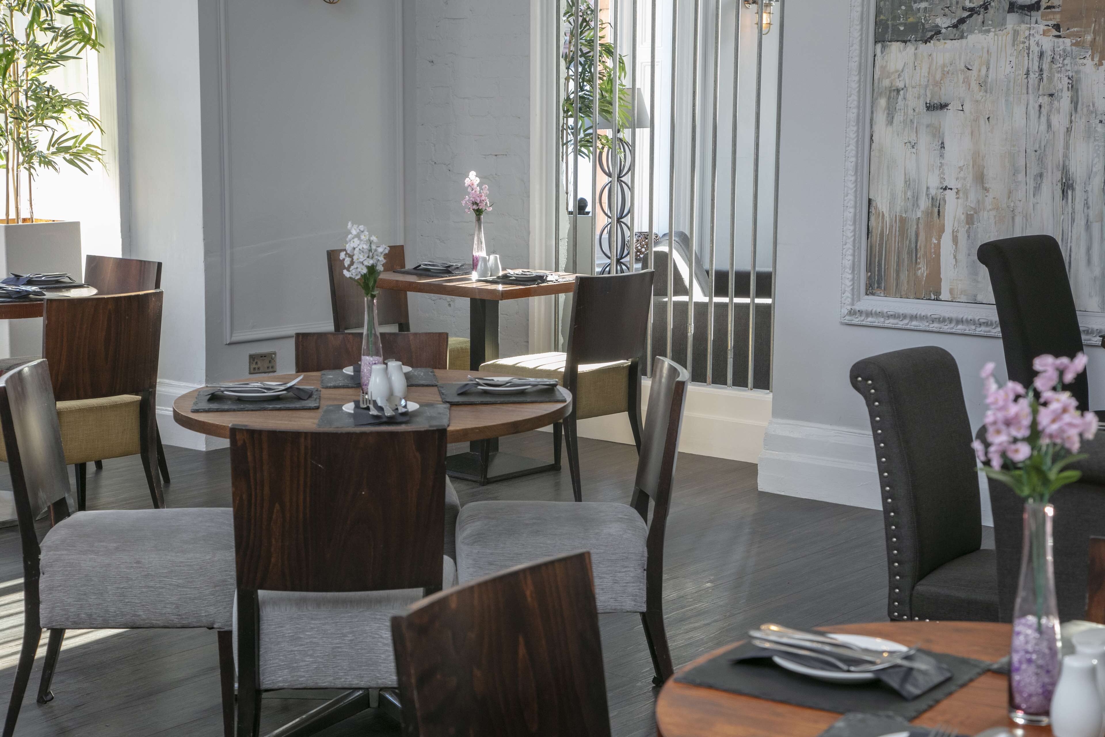 Un comedor con mesas redondas, sillas y un jarrón de flores.