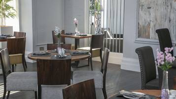 Un comedor con mesas redondas, sillas y un jarrón de flores.