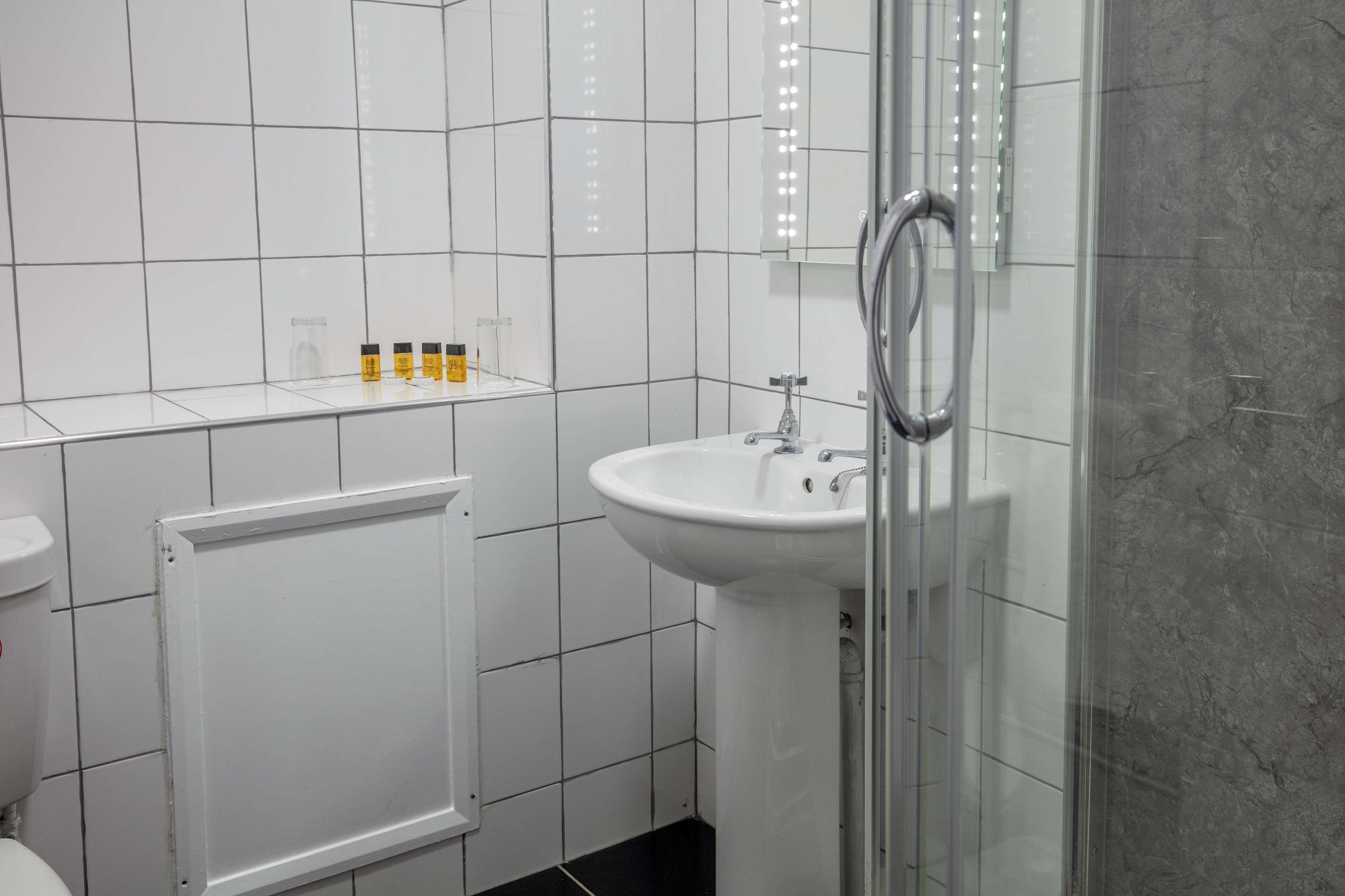 Um banheiro com pia branca, box de vidro e radiador branco.