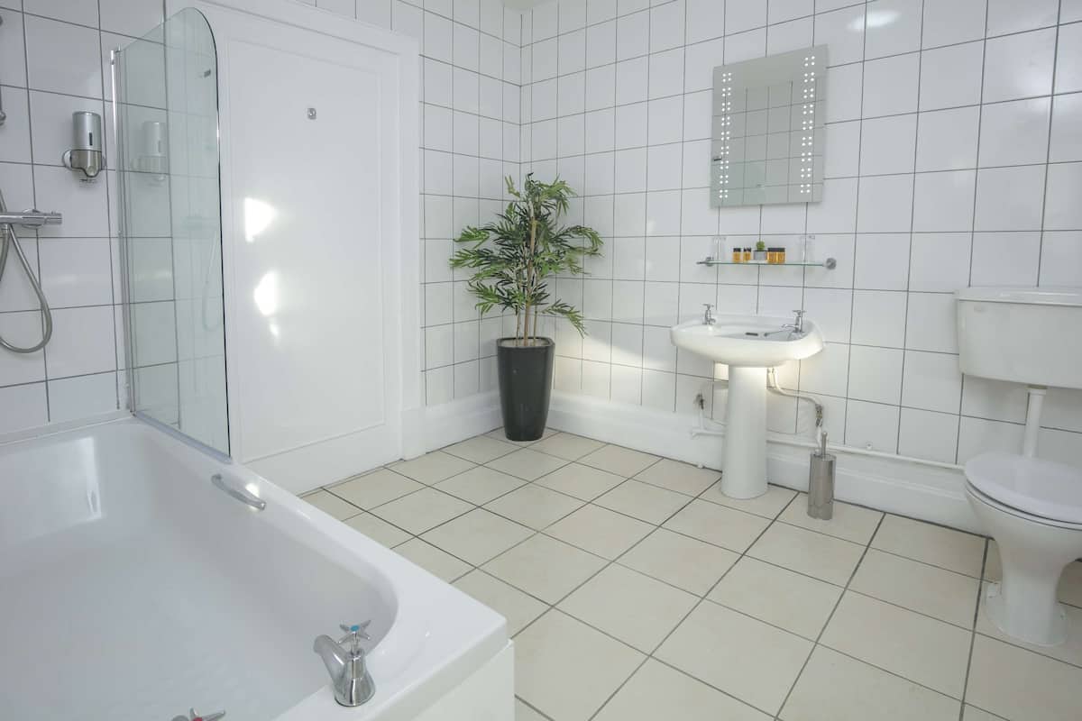 A modern bathroom with a bathtub, a sink, a toilet, and a potted plant.