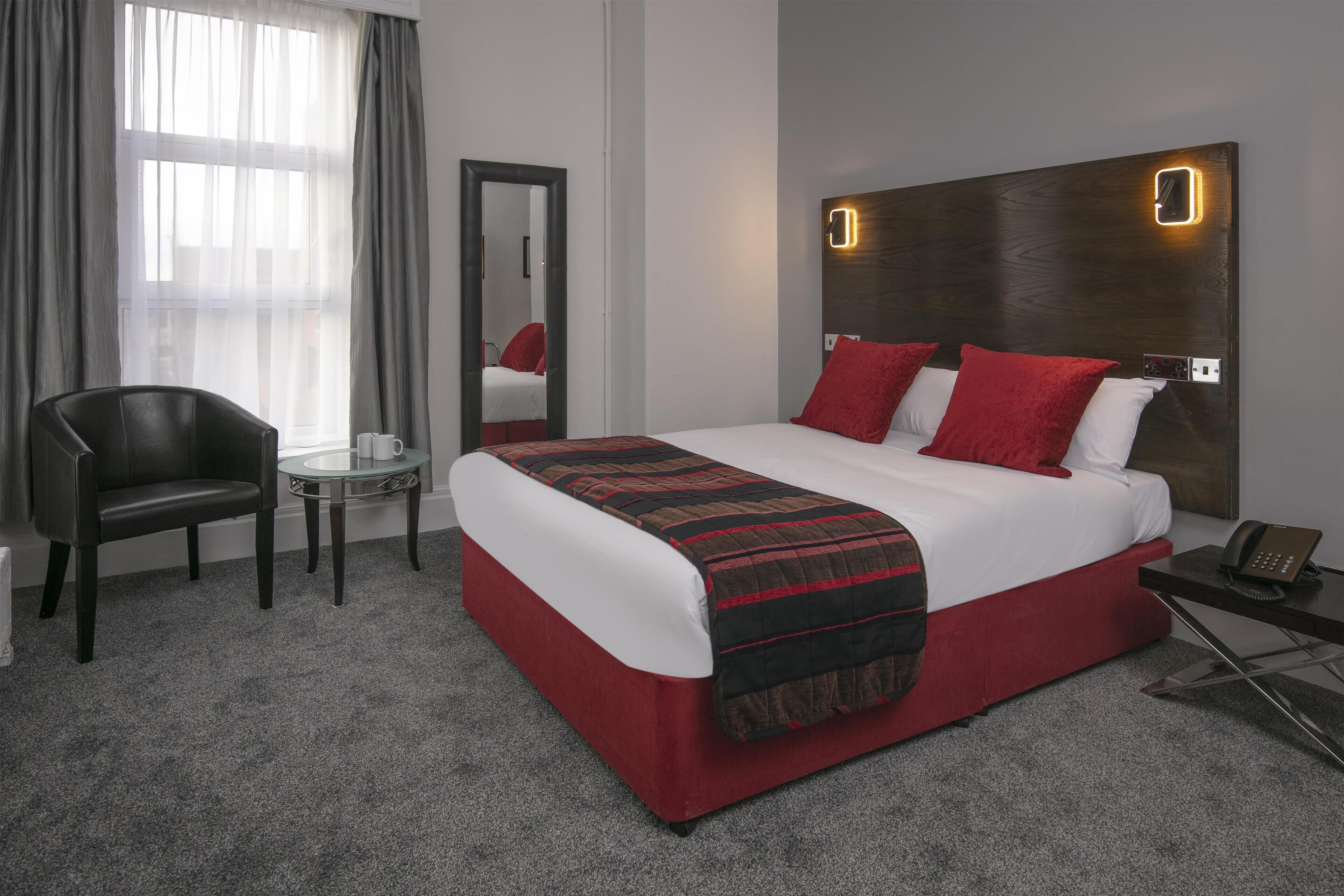A hotel room with a bed, a chair, a small table, and a mirror.