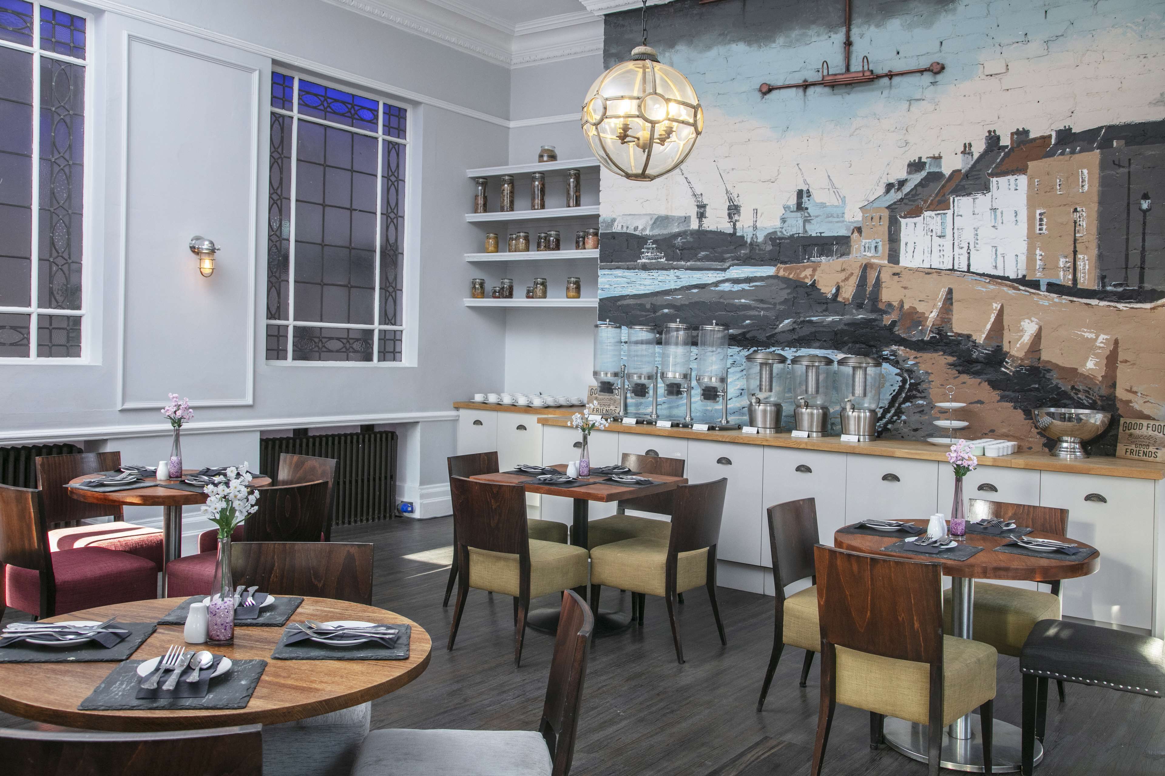 A dining area with round tables, chairs, and a mural of a coastal scene.