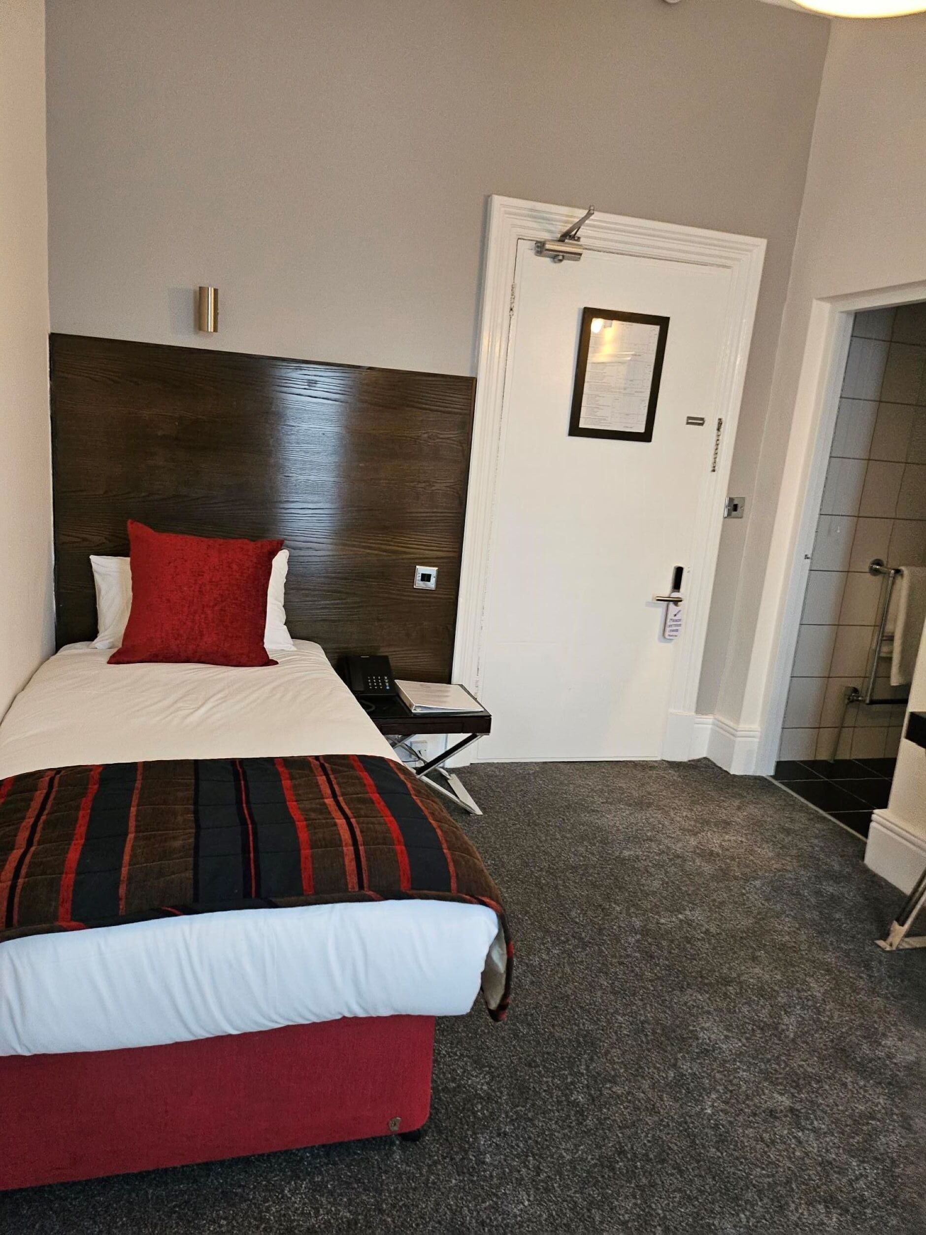 Una habitación de hotel con cama, escritorio, teléfono y puerta.