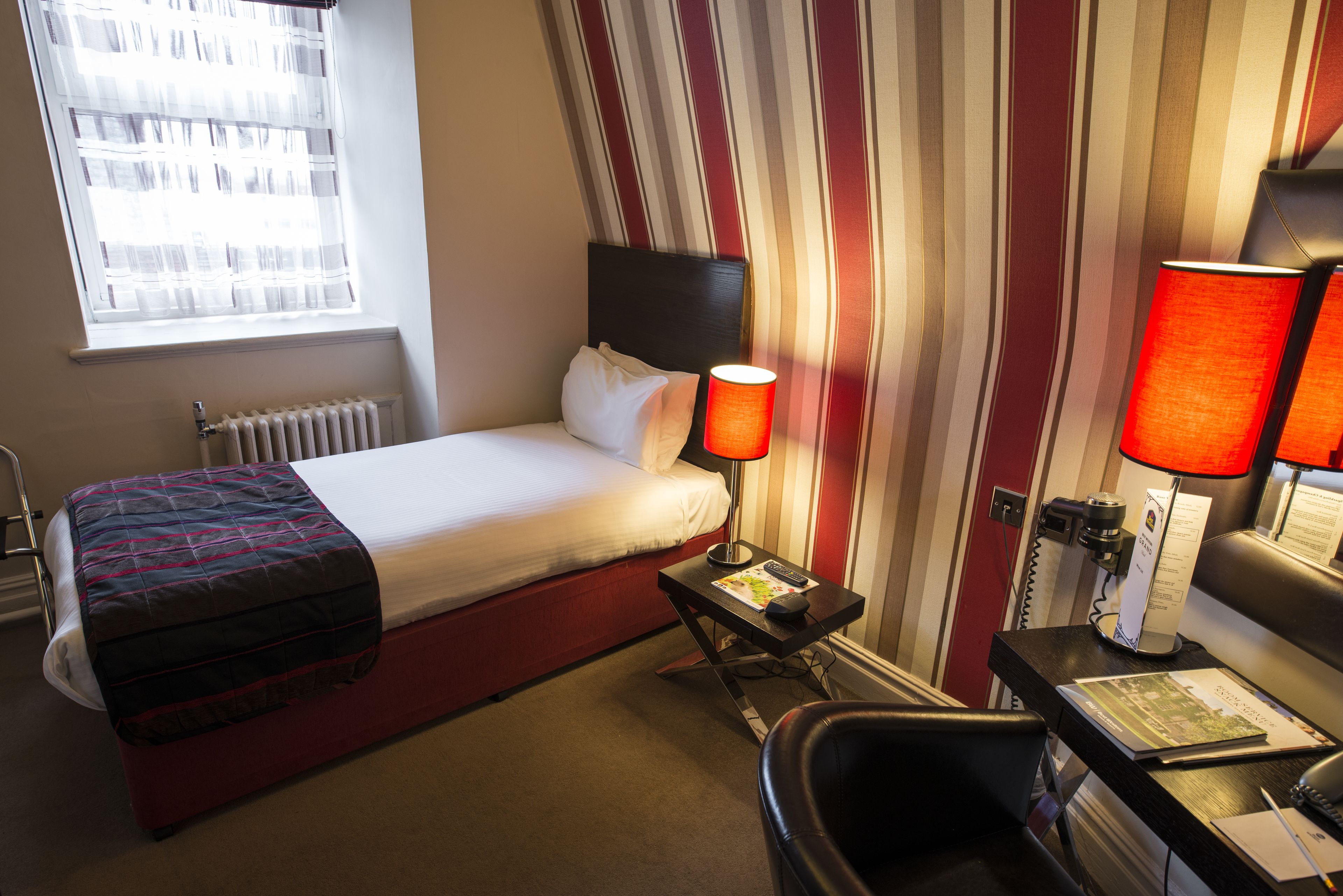 Una habitación de hotel con cama, escritorio, silla, lámpara y ventana.