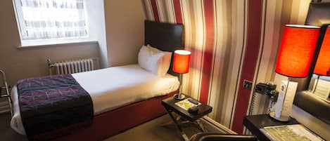 Una habitación de hotel con cama, escritorio, silla, lámpara y ventana.