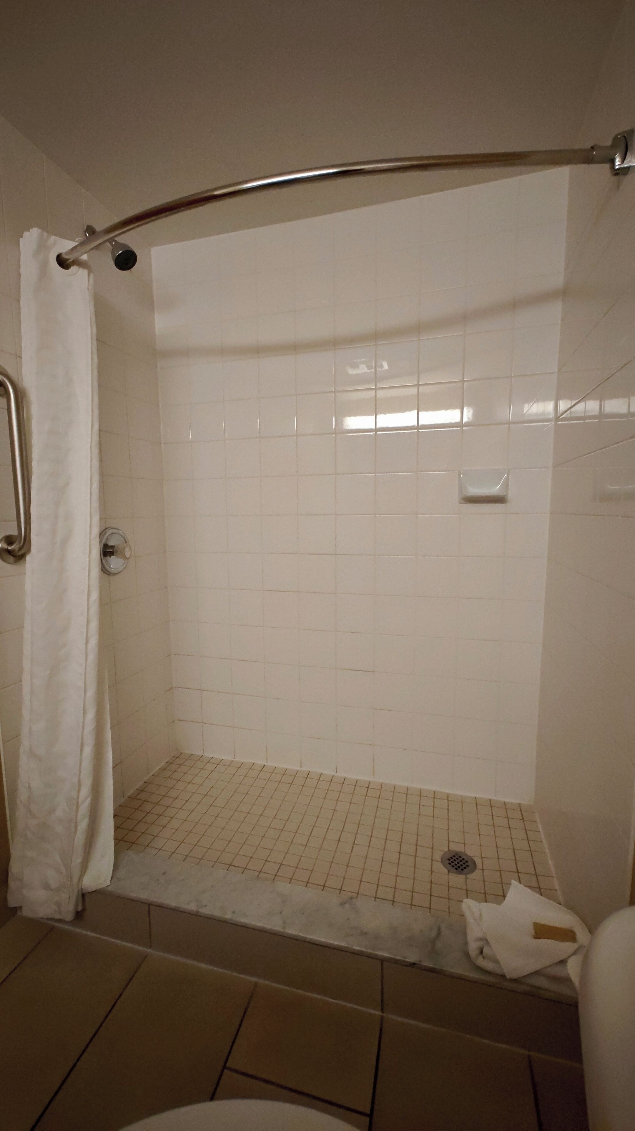 A shower area with a white tiled wall, a metal showerhead, and a white shower curtain.