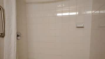 A shower area with a white tiled wall, a metal showerhead, and a white shower curtain.