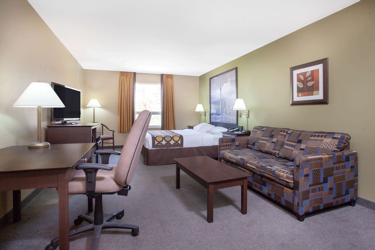 A hotel room with a bed, a sofa, a desk with a chair, a TV, and two lamps.