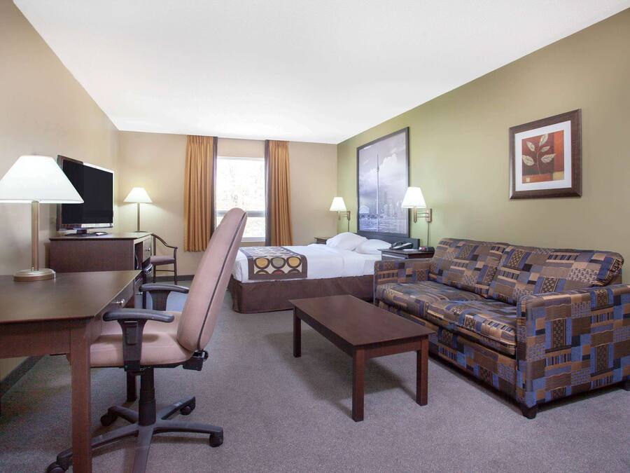 A hotel room with a bed, a sofa, a desk with a chair, a TV, and two lamps.