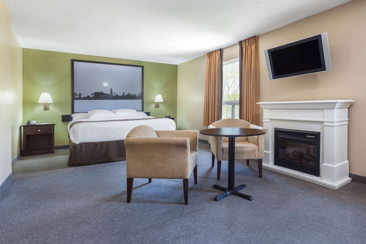 A hotel room with a bed, two chairs, a small table, a TV, and a fireplace.
