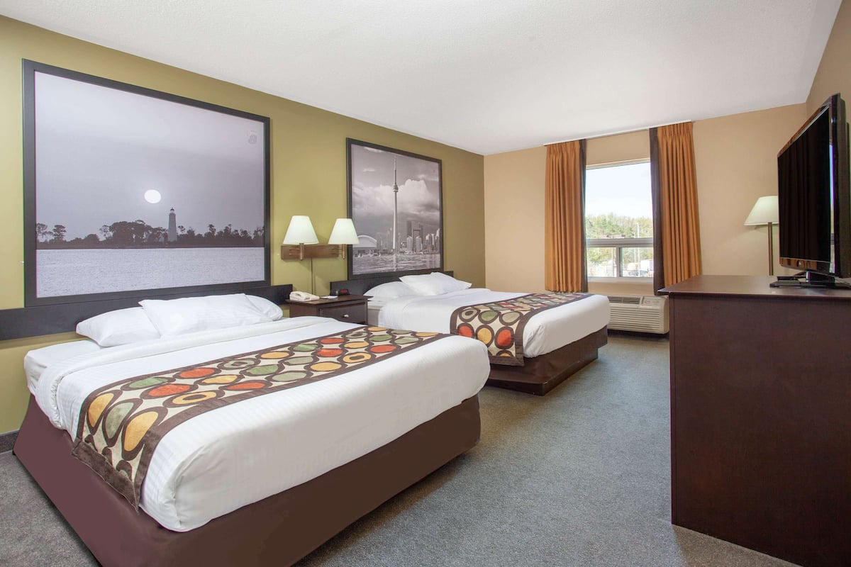 A hotel room with two beds, a desk, a television, and large windows.