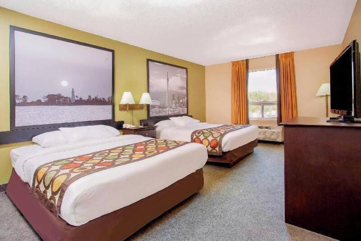 A hotel room with two beds, a desk, a television, and two wall-mounted lamps.