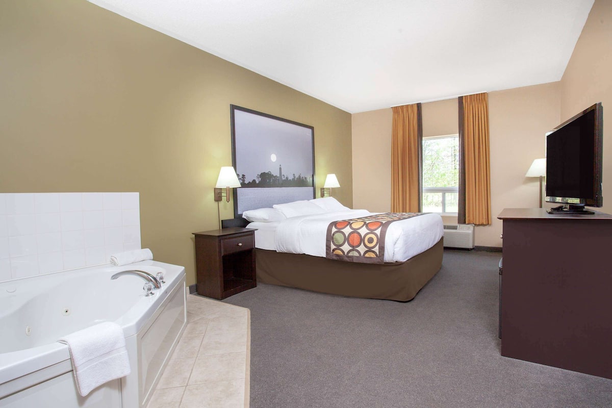 A hotel room with a large bed, a separate bathroom with a bathtub, a television, and a window with curtains.